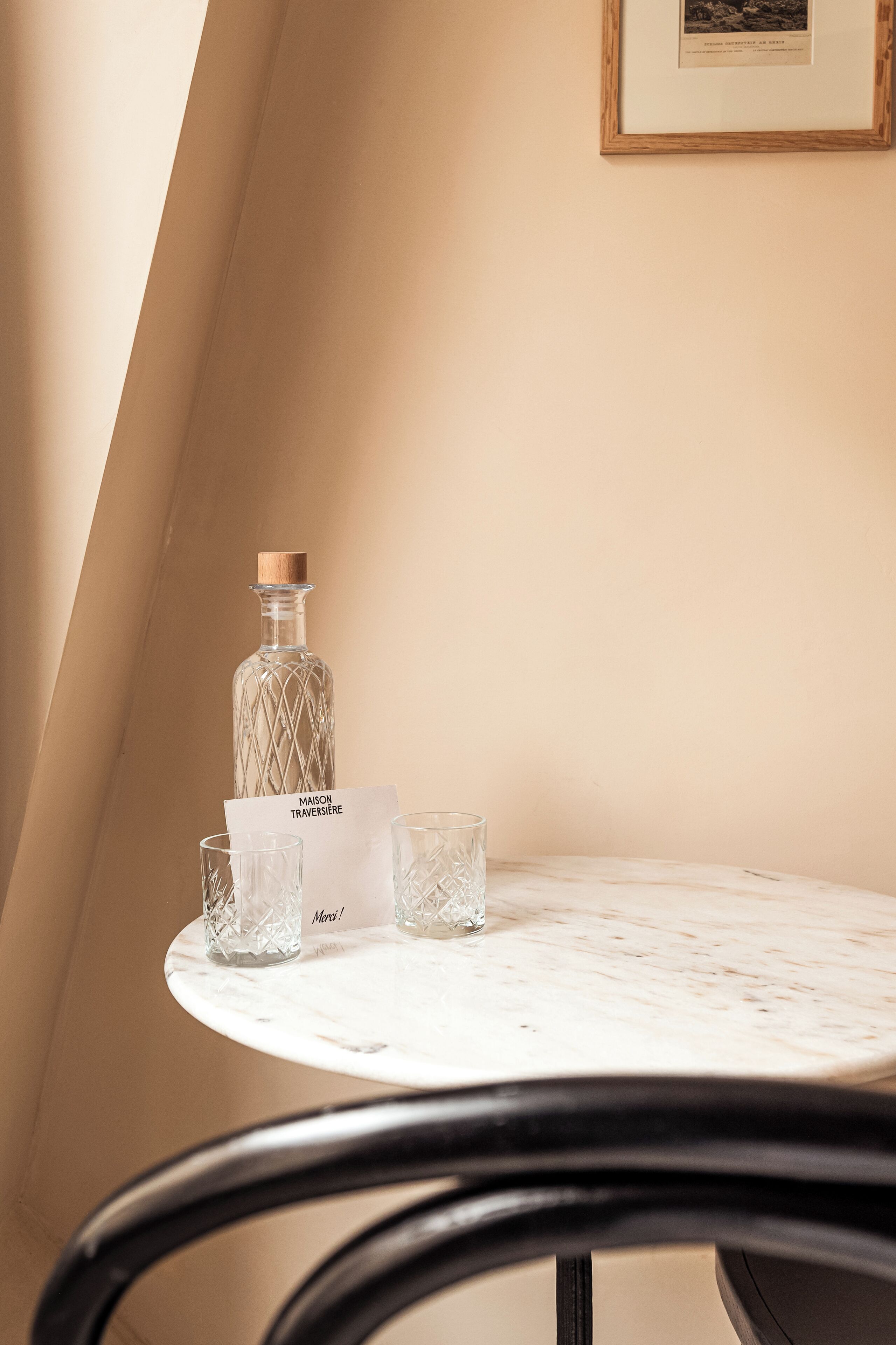 A table with a bottle and glasses, a menu, and a framed picture on the wall.