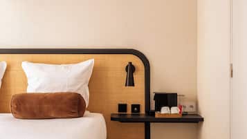 Habitación de hotel con cama, almohadas, mesita de noche con lámpara, un altavoz pequeño y cafetera.