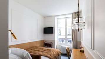 A hotel room with a bed, a desk, a chandelier, a television, and a window with curtains.