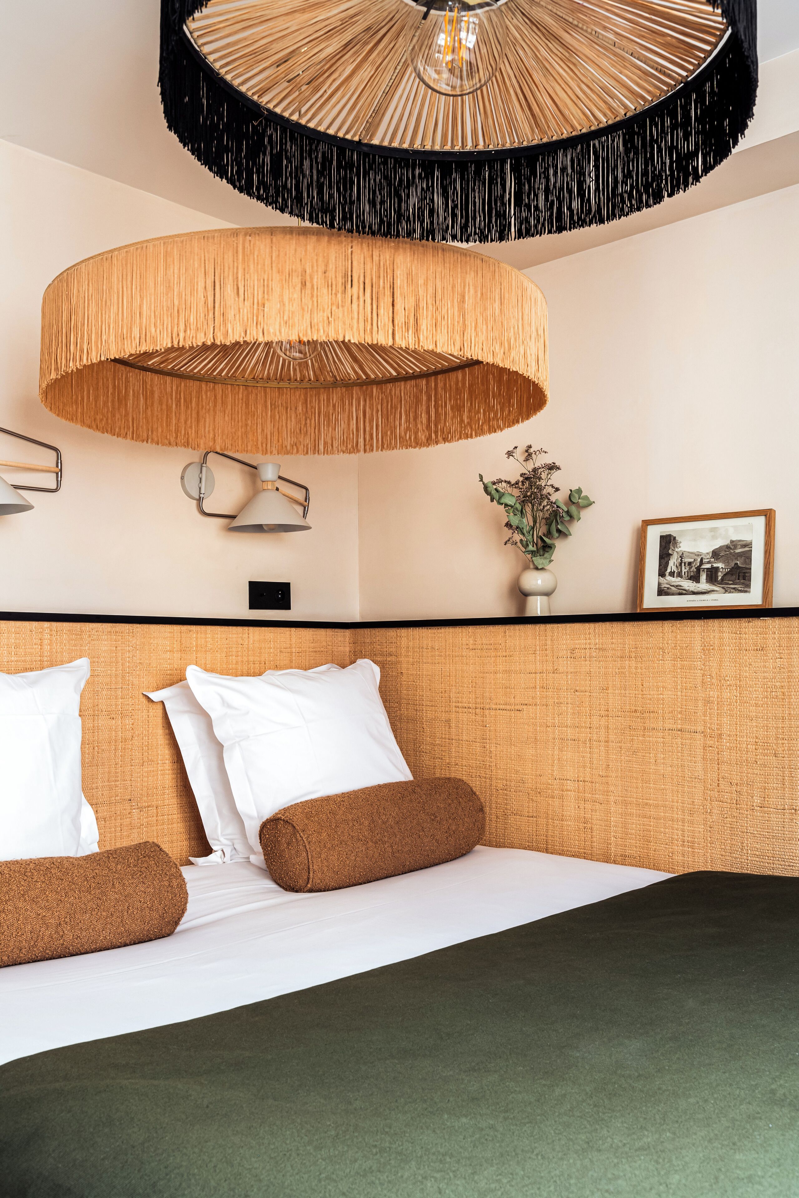 A hotel room with a bed, a wall-mounted light fixture, a small plant, and a framed picture.