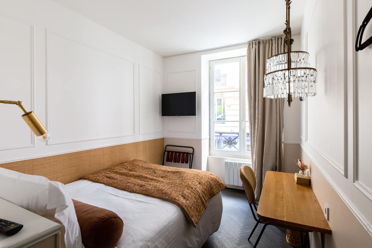 Ein Hotelzimmer mit Bett, Nachttisch, Lampe, Fernseher und einer Chandelier.