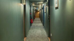 Un largo y estrecho pasillo de hotel con puertas a ambos lados, alfombra estampada e iluminación en el techo.