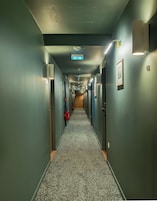 Un largo y estrecho pasillo de hotel con puertas a ambos lados, alfombra estampada e iluminación en el techo.