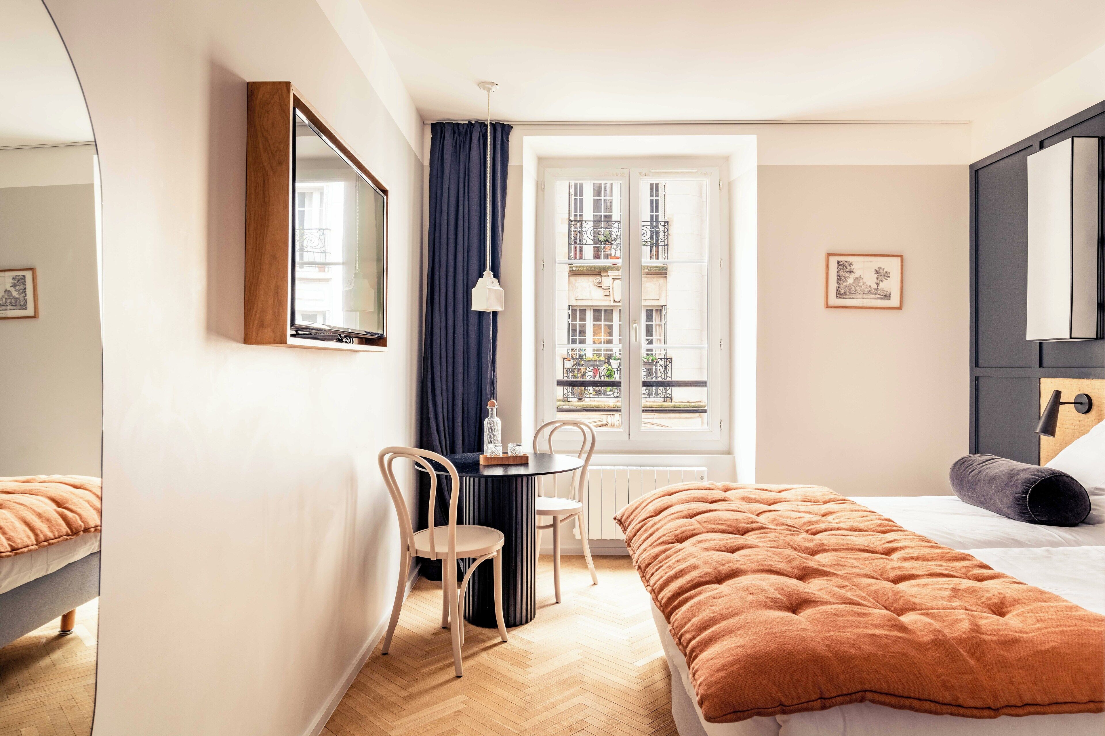 Ein Hotelzimmer mit Bett, Schreibtisch, Stuhl, Fenster mit Blick auf Gebäude und Heizkörper.