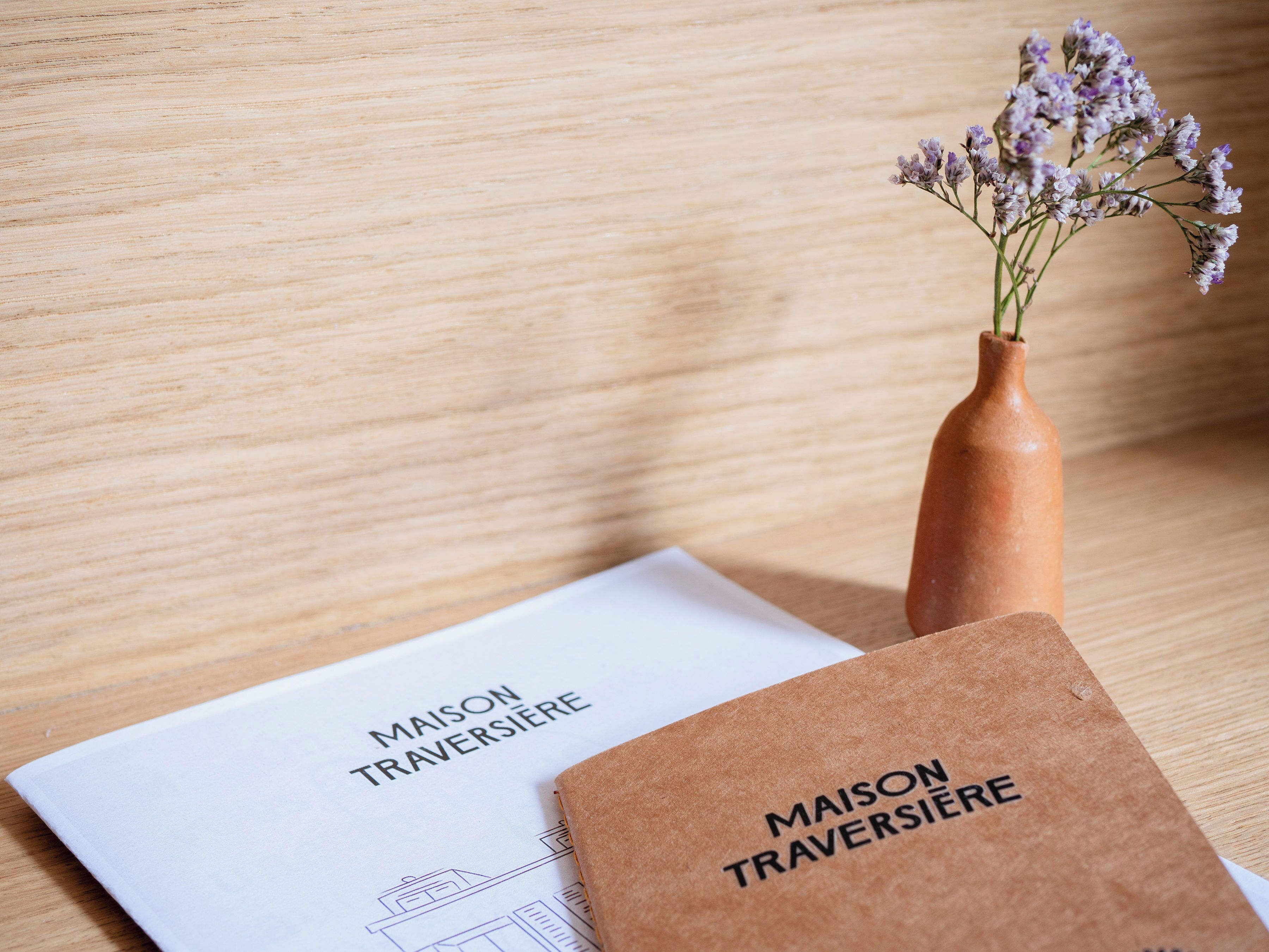 Una superficie in legno con una busta di carta marrone etichettata "MAISON TRAVERSIERE" e un foglio di carta con lo stesso testo.
