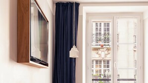 Una habitación con cama, una mesa con sillas, un ventanal con cortinas y un televisor instalado en la pared.