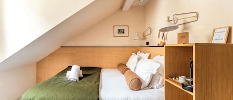 Una habitación de hotel con una cama, una manta verde, una mesita de noche de madera con una lámpara y un cartel enmarcado en la pared.