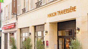 Un edificio con un letrero que dice "MAISON TRAVERSIÈRE" y macetas con plantas en la entrada.