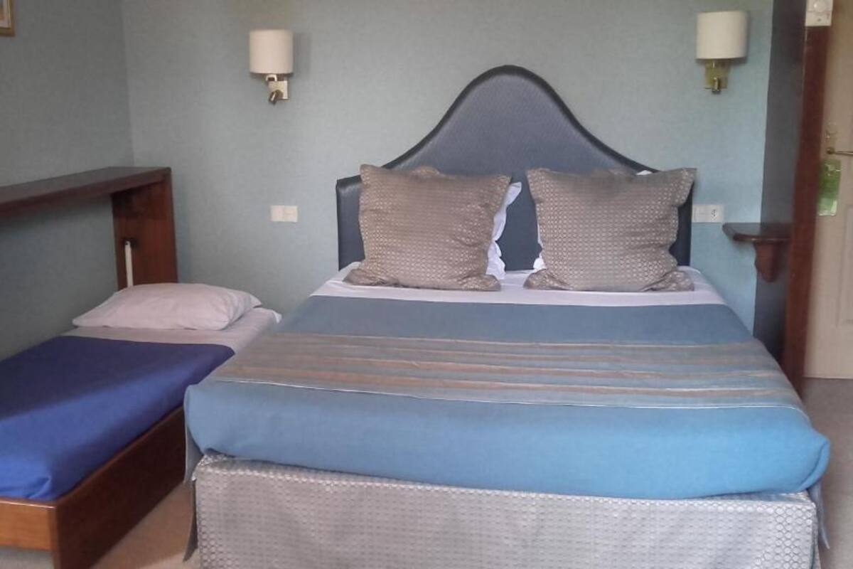 Een enkel bed met een blauw-witte streep dekbed, twee kussens en een hoofdbord.