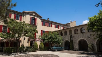 A hotel with a courtyard, red shutters, and a car parked in front.