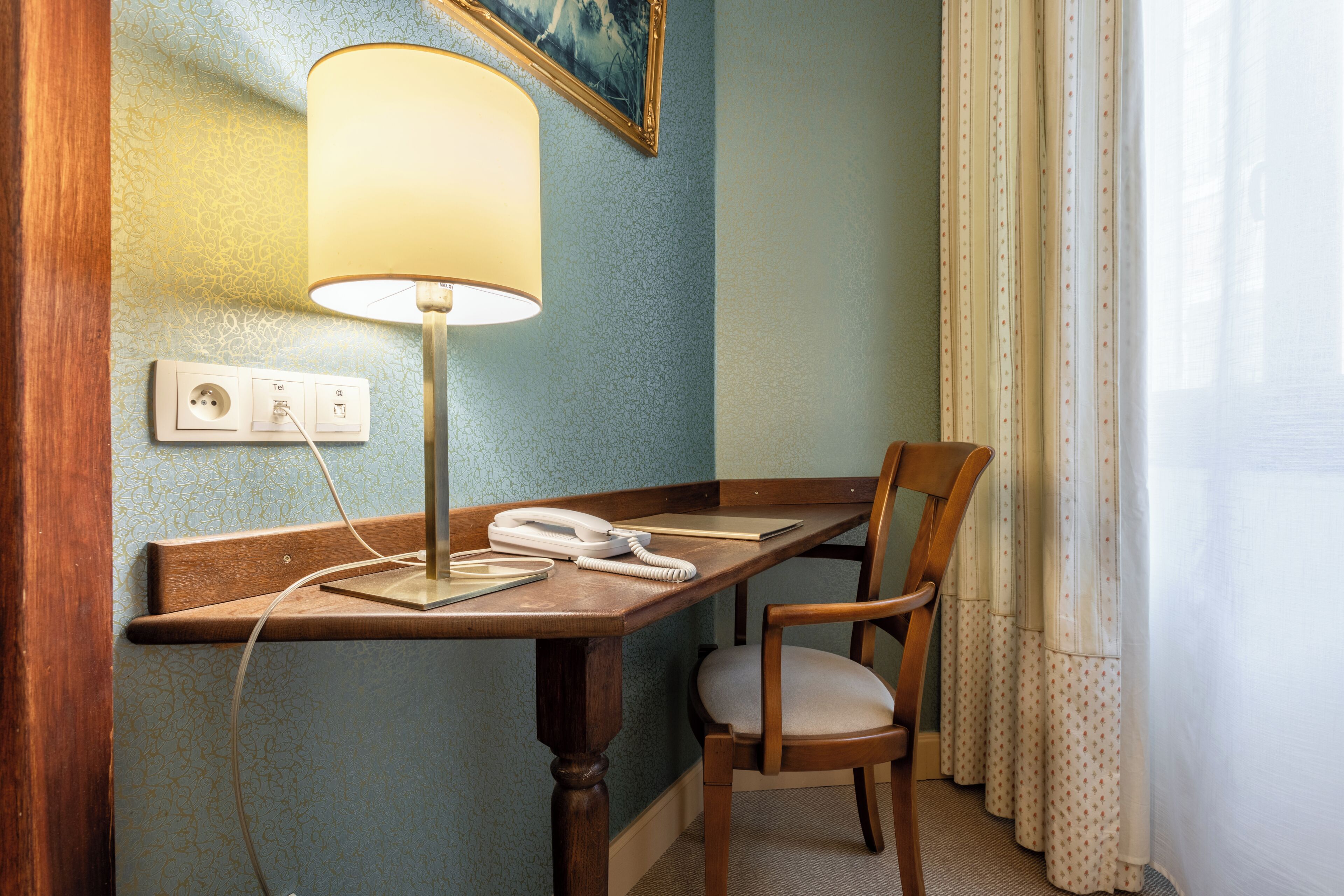 Een hotelkamer met een houten bureau, een telefoon, een lamp en een stoel.