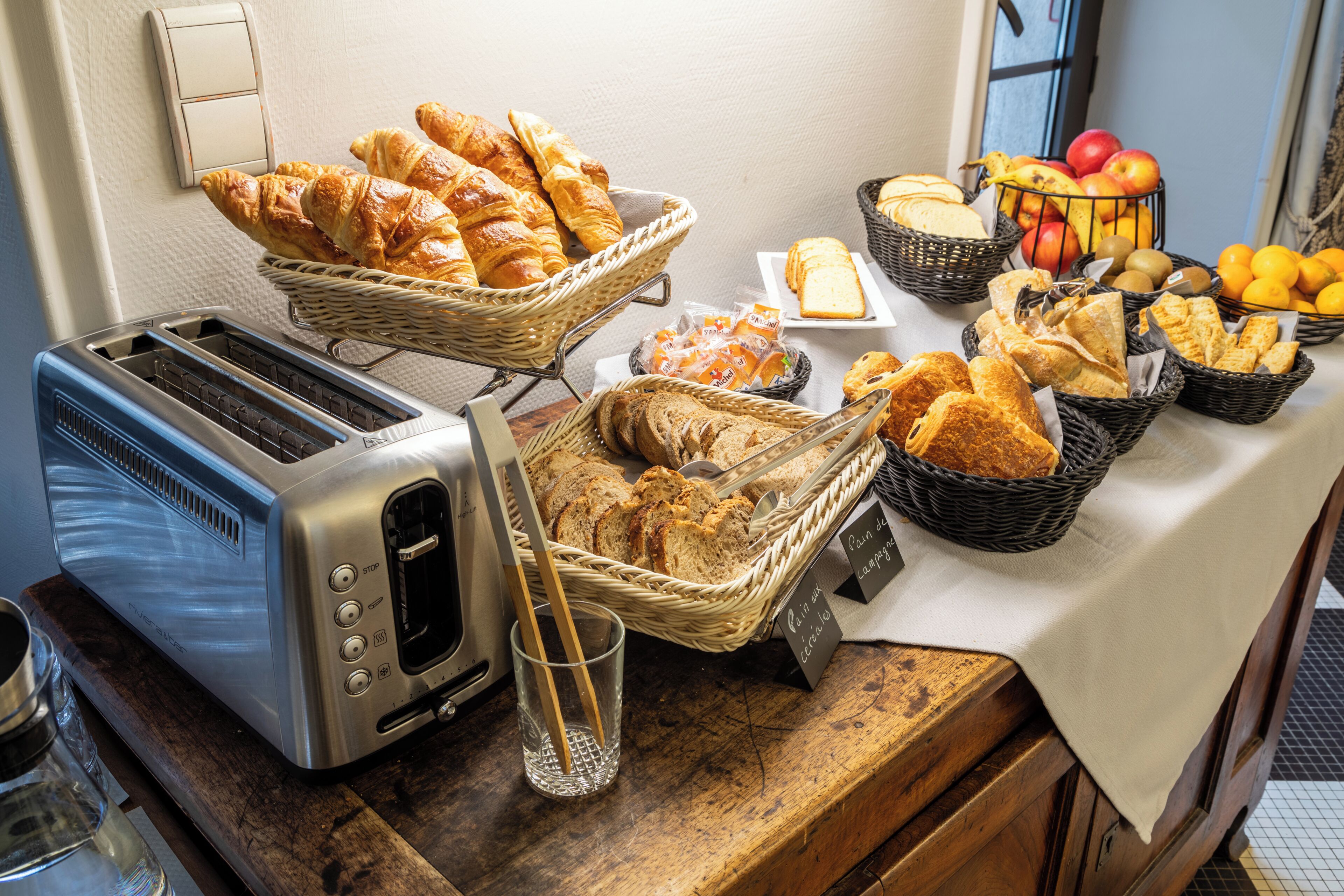 A breakfast buffet with various breads, pastries, and fruits.