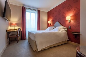 Une chambre d’hôtel équipée d’un lit, d’un bureau, d’une chaise et d’un téléviseur fixé au mur.