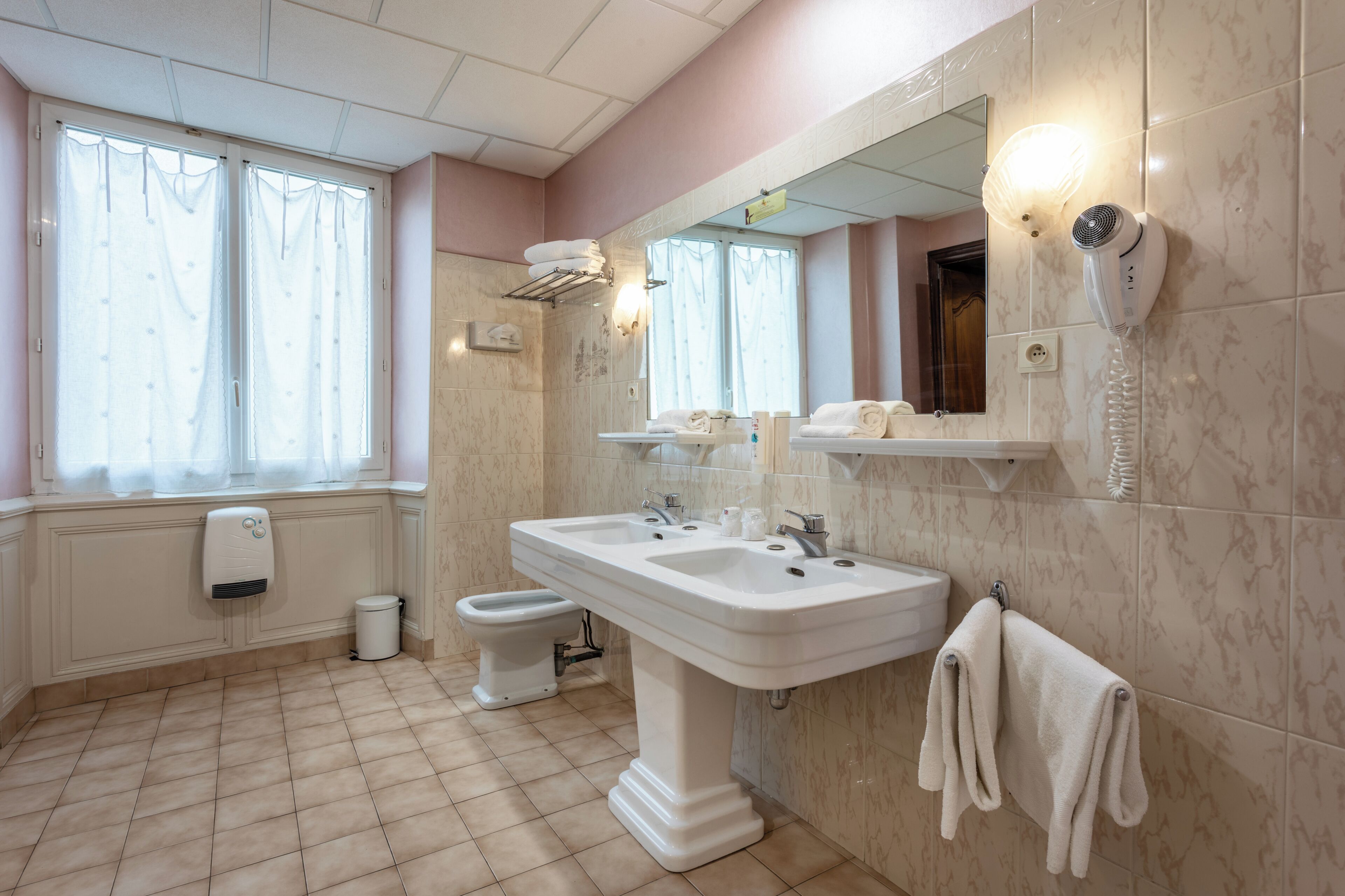 Een badkamer met een wastafel op voetstuk, toilet, bidet, handdoekhouder, spiegel en haardroger.