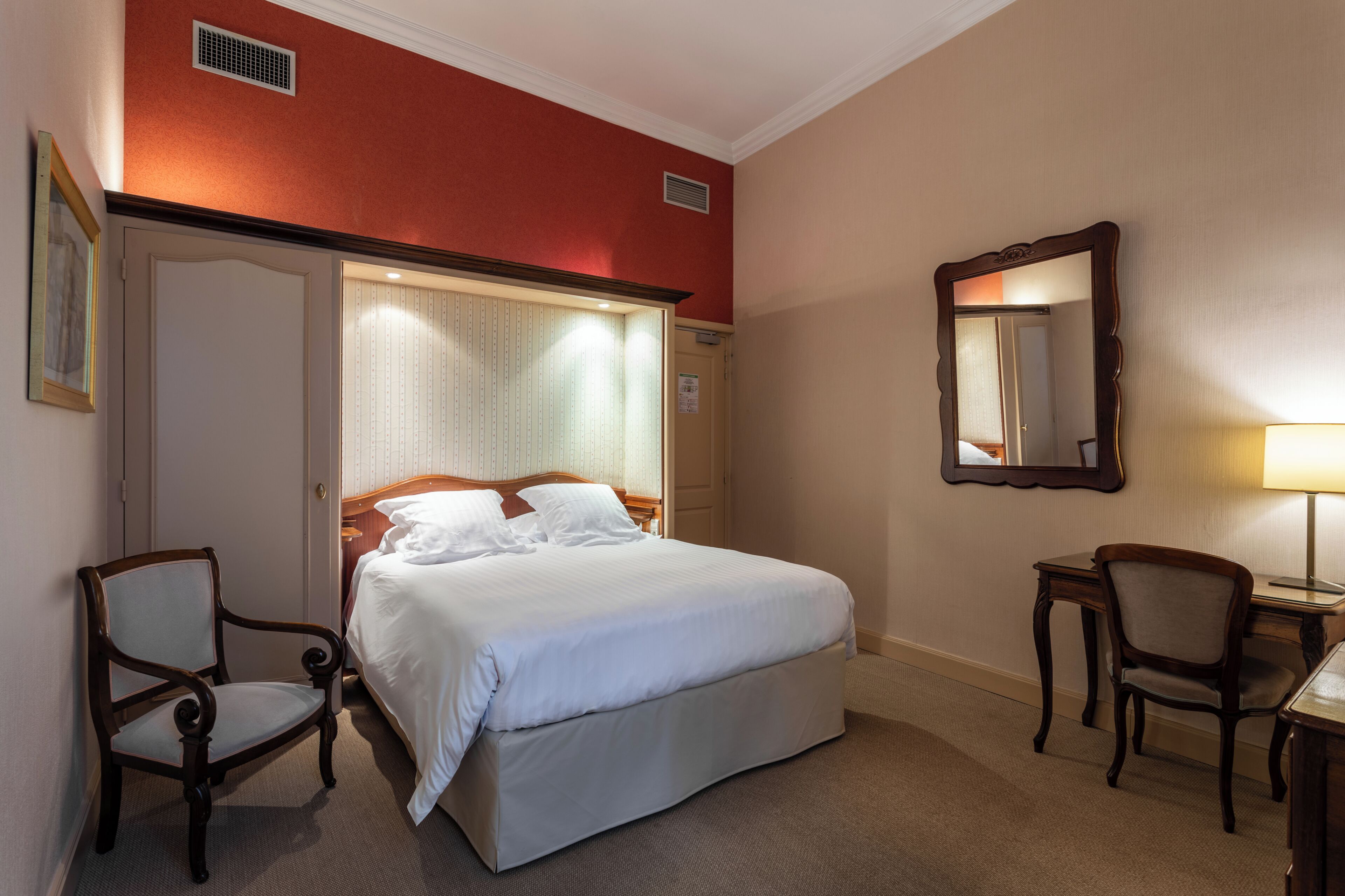 Une chambre d’hôtel avec un grand lit, deux chaises, un bureau et un miroir.