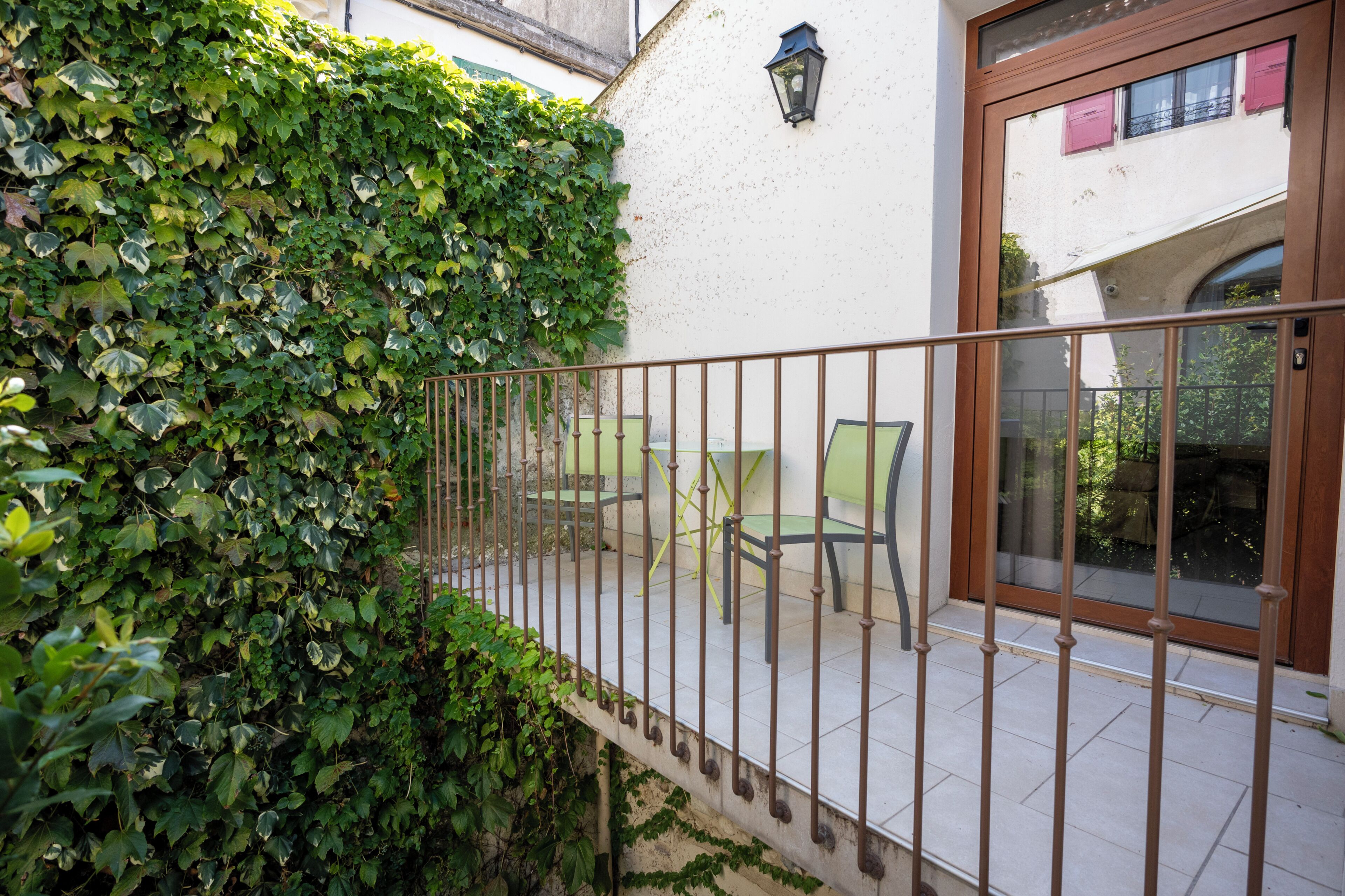 Un balcon avec une rambarde en métal, un mur blanc et un mur recouvert de lierre vert.