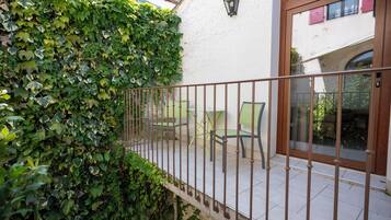 Un balcon avec une rambarde en métal, un mur blanc et un mur recouvert de lierre vert.