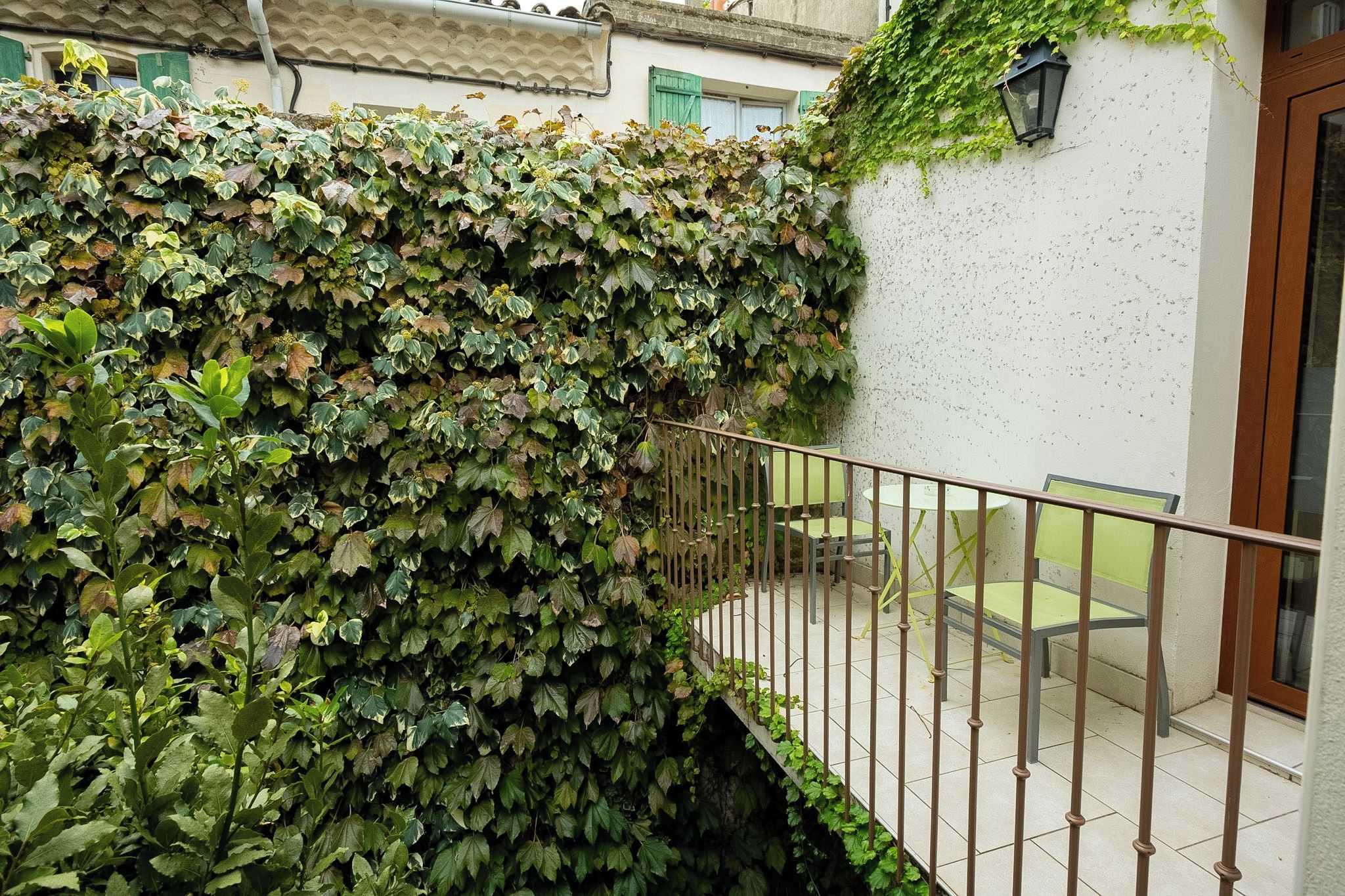 A balcony with a metal railing, a white wall, and a green plant wall.