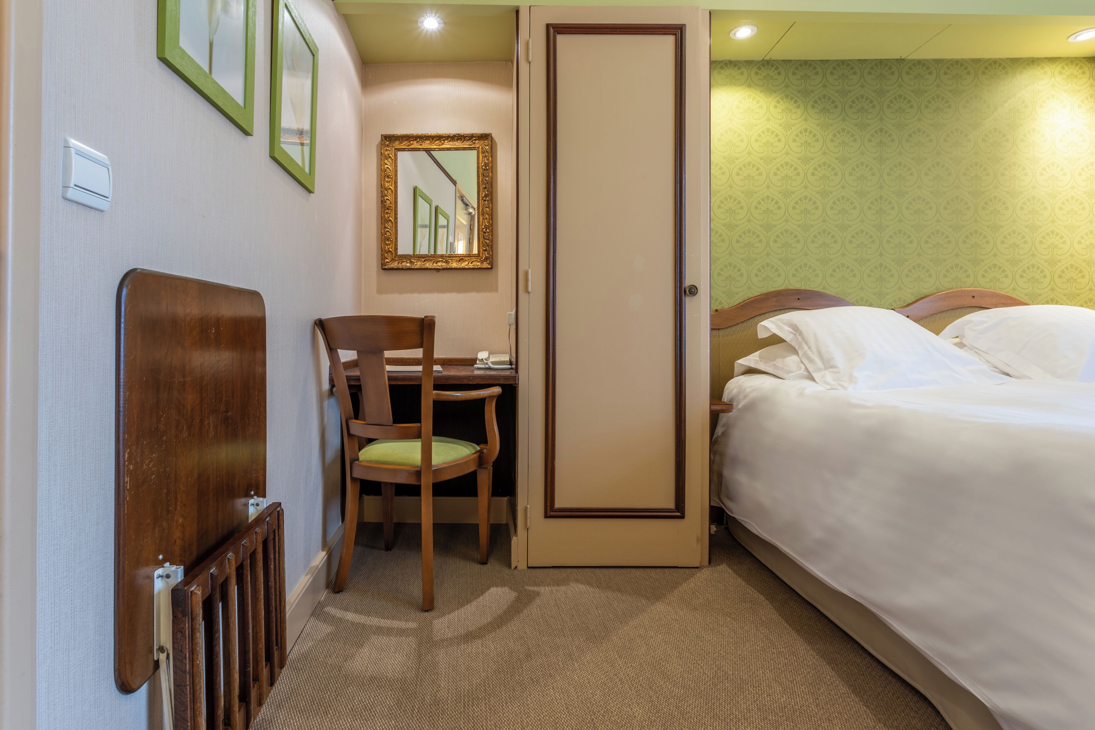 A hotel room with a bed, a desk, a chair, and a door.