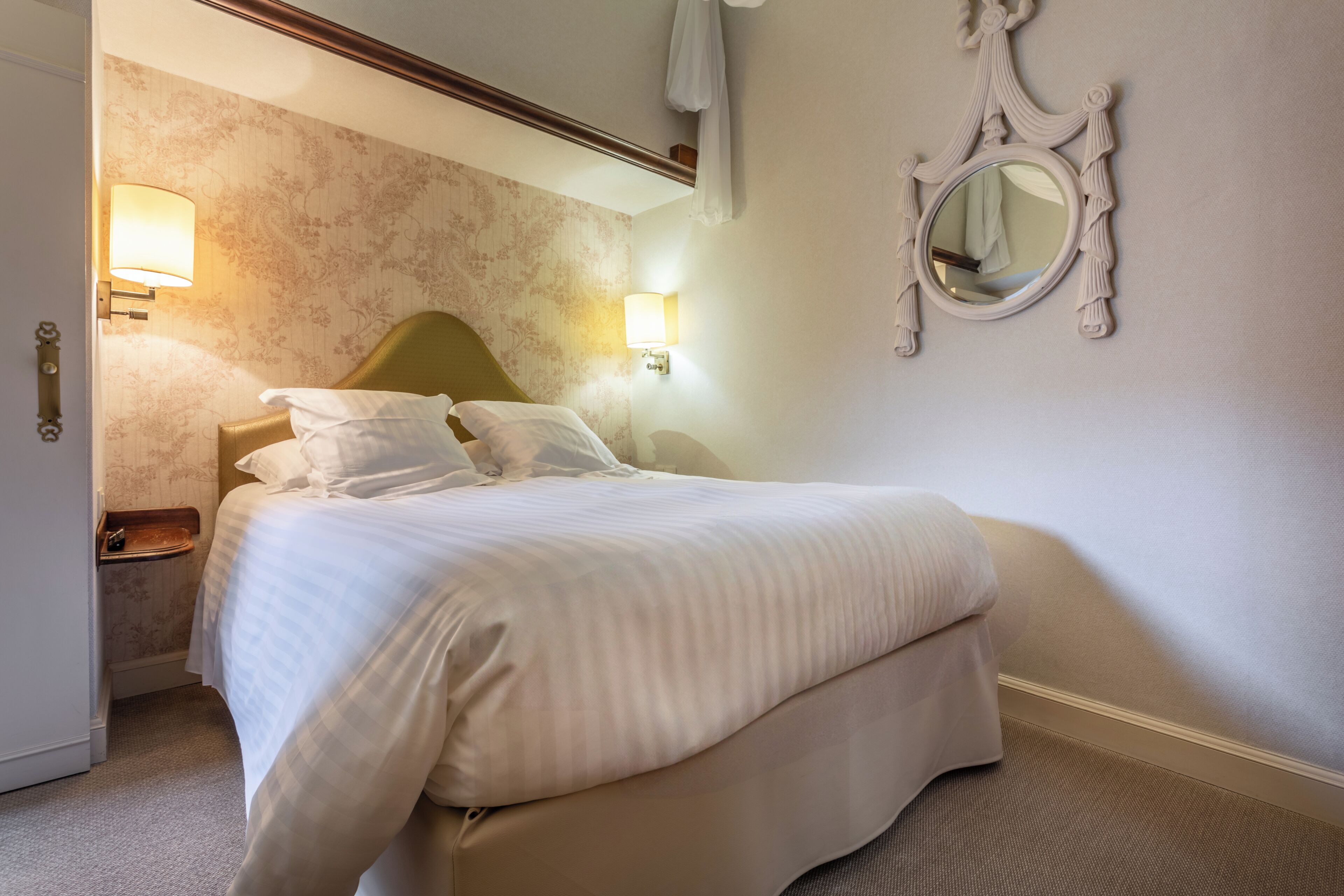 Een hotelkamer met een bed, twee bedlampjes, een spiegel en een deur.