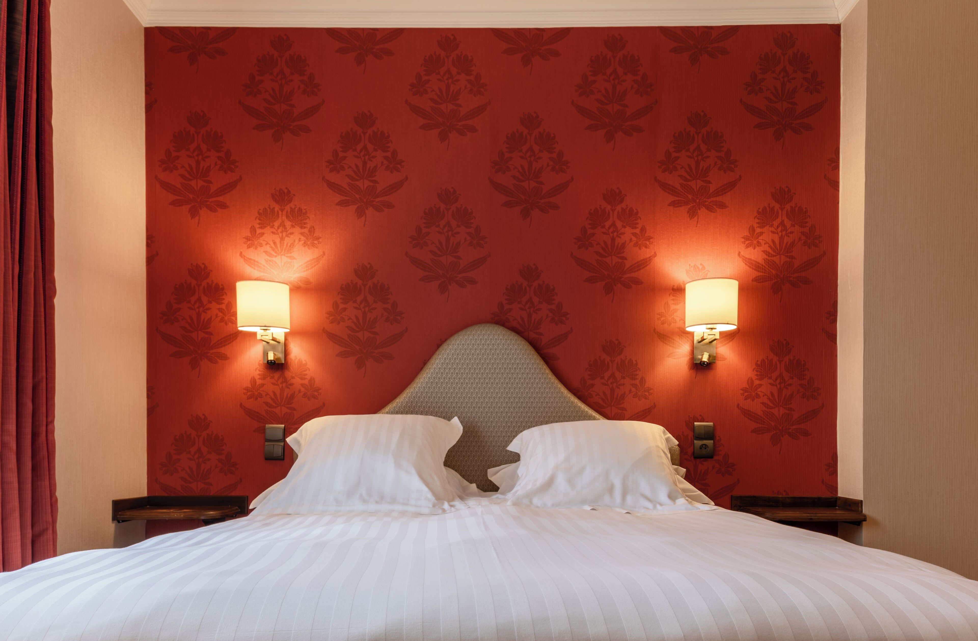 Habitación de hotel con una cama grande, dos lámparas de pared y un papel tapiz estampado con motivos florales.