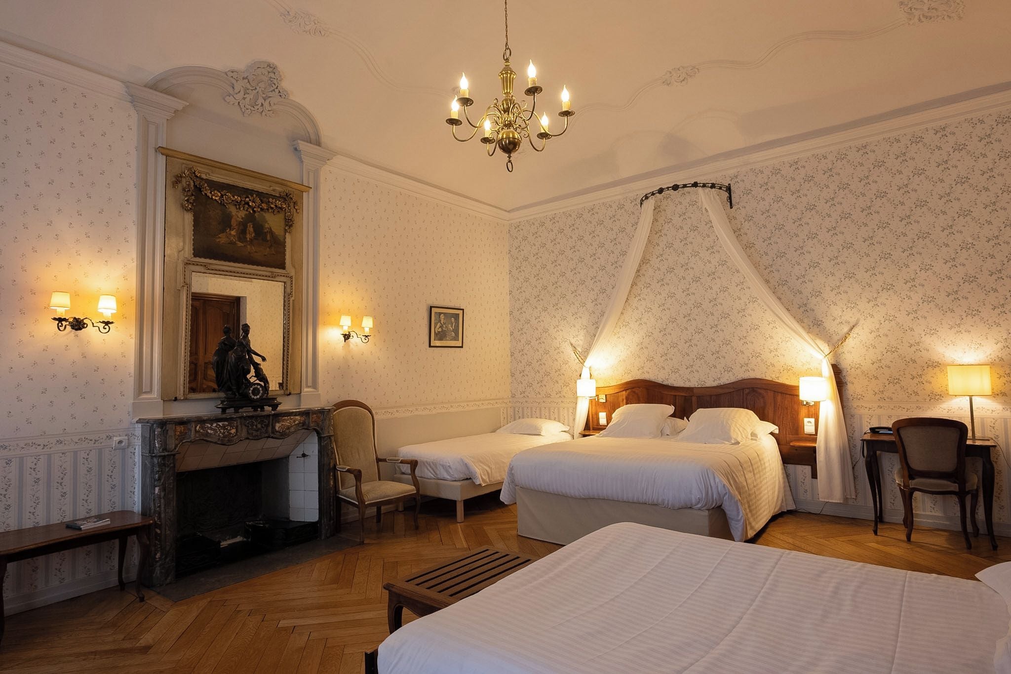 Habitación de hotel con chimenea, dos camas, dosel sobre la cama y un escritorio con una silla.