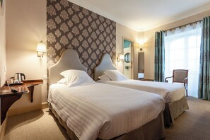 A hotel room with two beds, a desk with a lamp, a chair, and a view of the outdoors. - Citotel Le Sphinx (Montélimar)