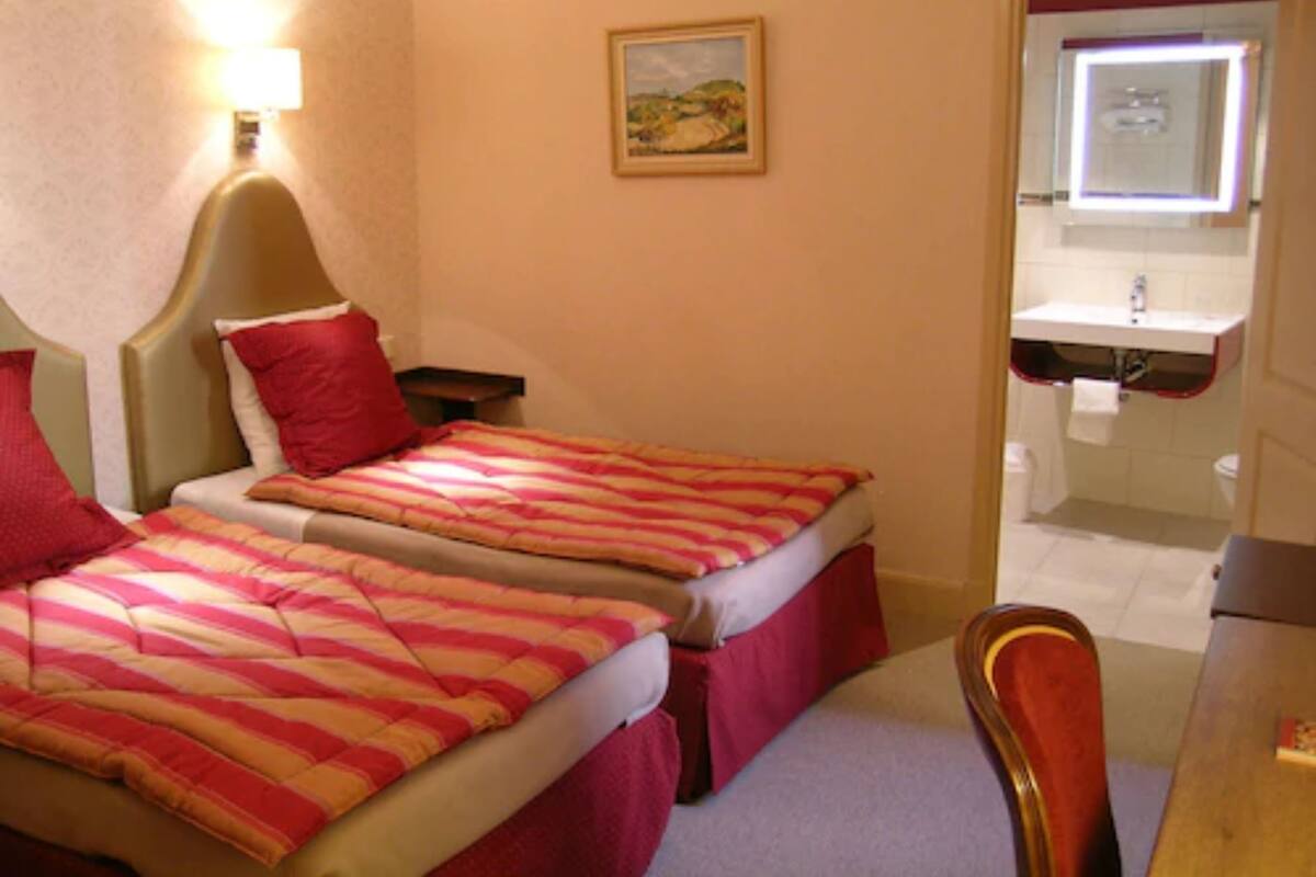 Een slaapkamer met een bed, nachtkastjes, een stoel, een schilderij en een badkamer die door een open deur zichtbaar is.