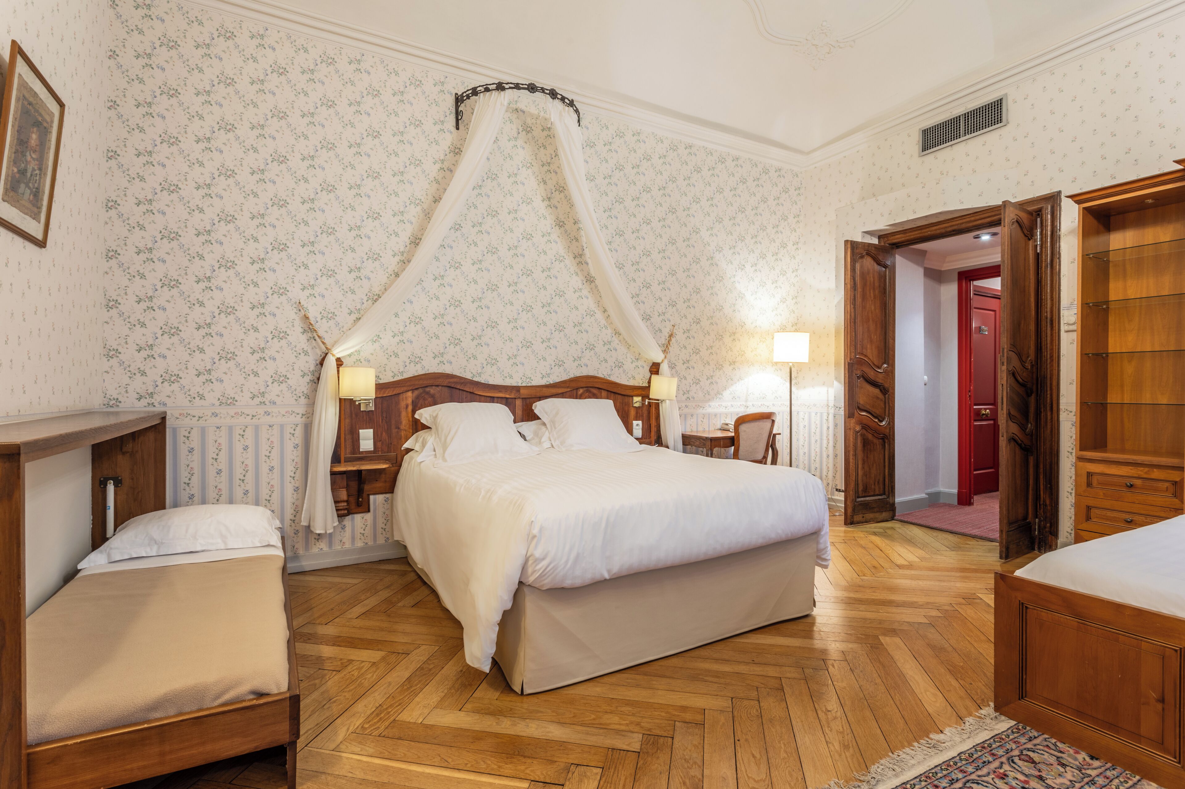 A bedroom with a four-poster bed, wooden flooring, and floral wallpaper.