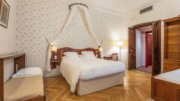 A bedroom with a four-poster bed, wooden flooring, and floral wallpaper.