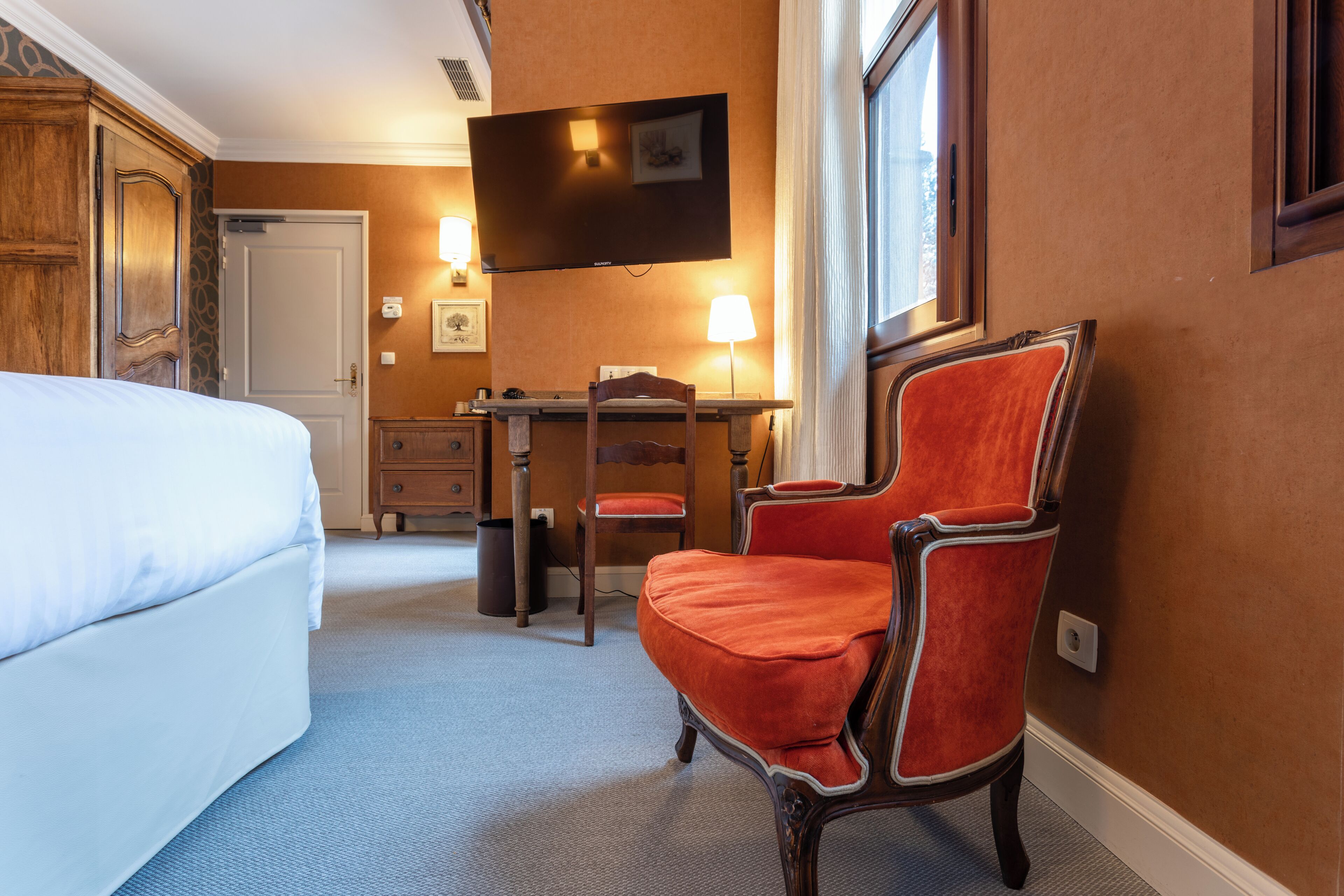 A hotel room with a bed, a desk, a chair, a television, and a window.