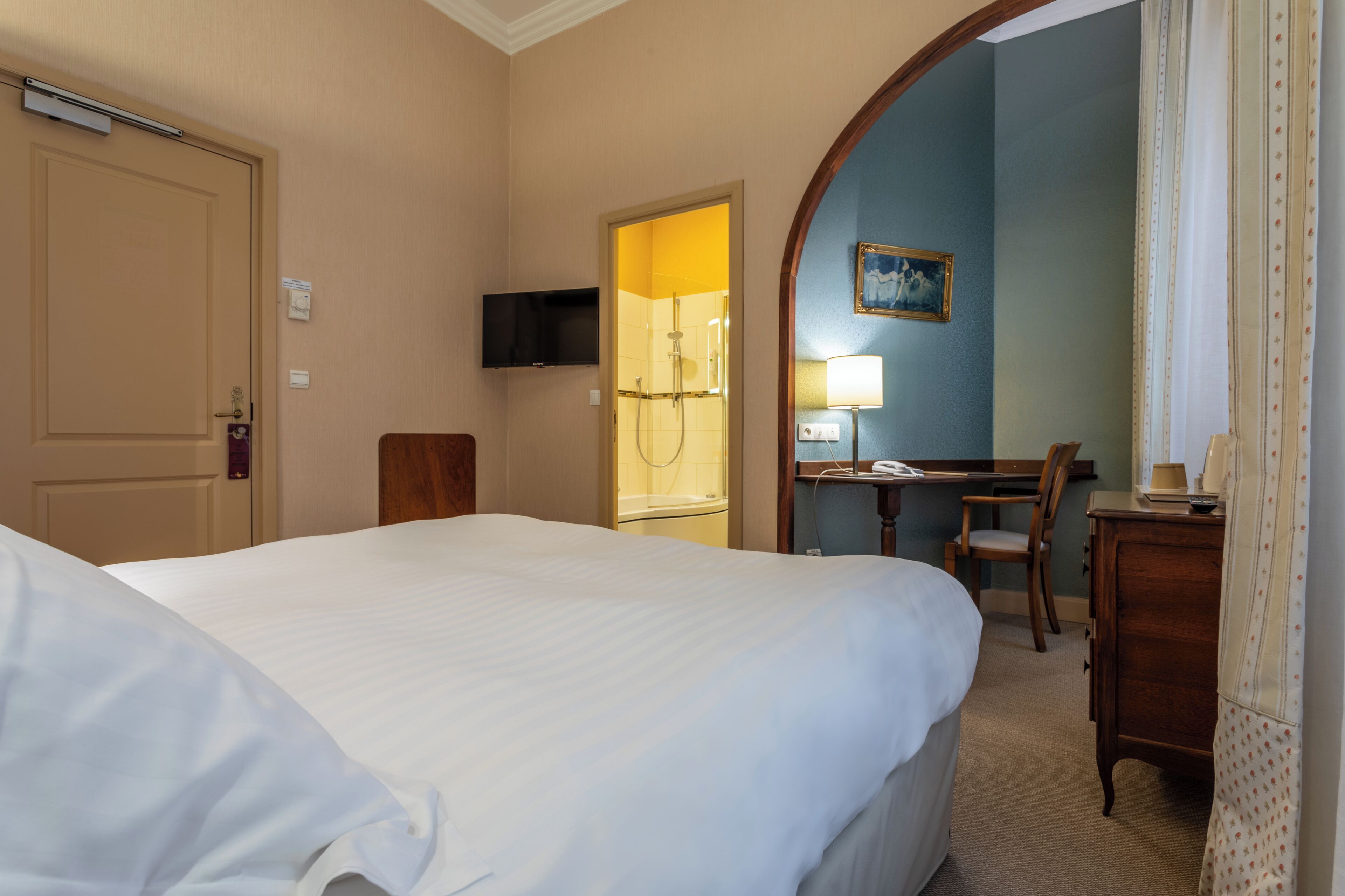 A hotel room with a bed, a desk with a chair, a television, and a bathroom with a shower.