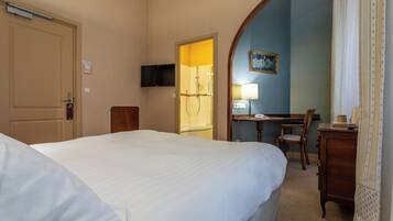 A hotel room with a bed, a desk with a chair, a television, and a bathroom with a shower.