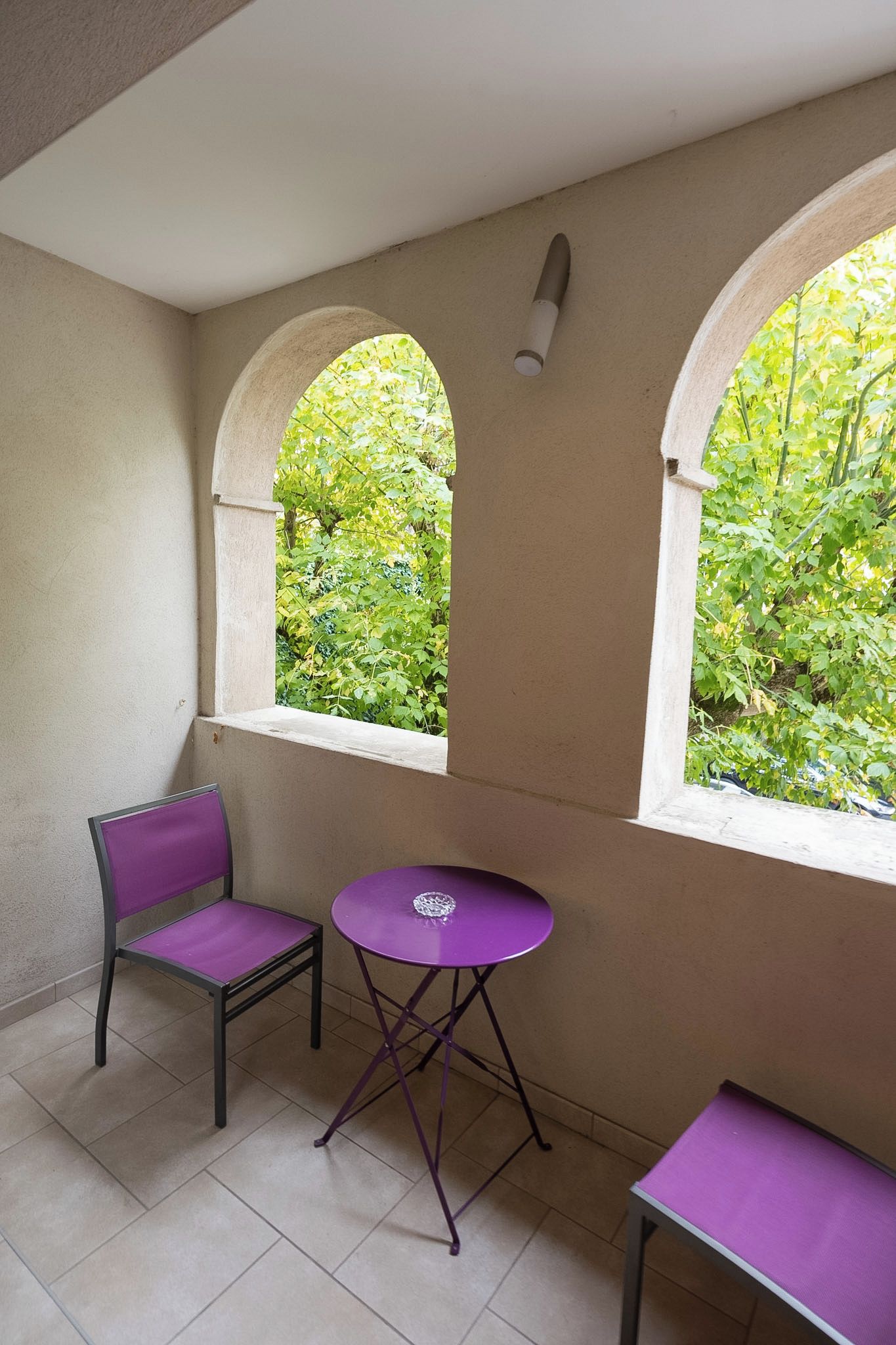 A room with two arched windows, a purple chair, a purple table, and a small table.