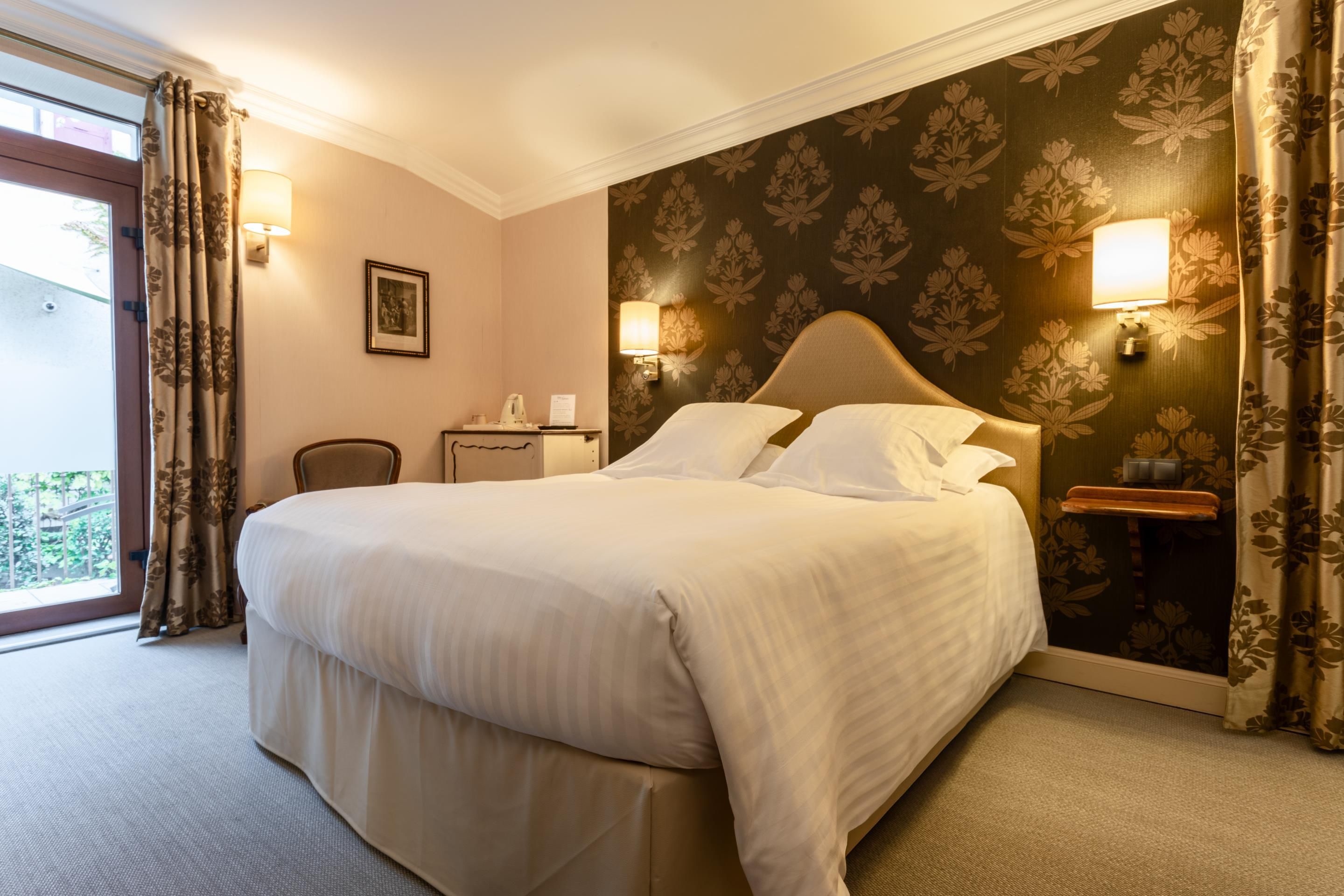 A hotel room with a large bed, two bedside lamps, a nightstand, a chair, and a window with curtains.