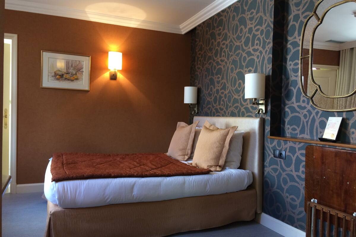 Een hotelkamer met een bed, twee wandlampen, een lijst met een afbeelding en een spiegel.