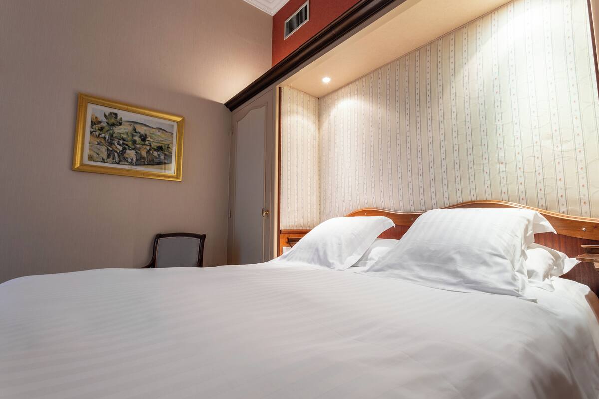 Een net opgemaakt bed met witte lakens in een hotelkamer, met een houten hoofdbord en een ingelijste foto aan de muur.