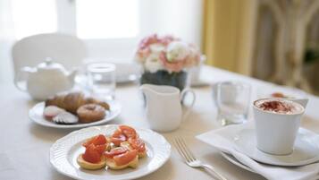 Desayuno con cruasanes, tomates en tostada y una taza de café sobre una mesa.