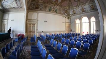 Un salón de conferencias con filas de sillas azules, un escenario con una mesa verde y detalles decorativos en el techo.