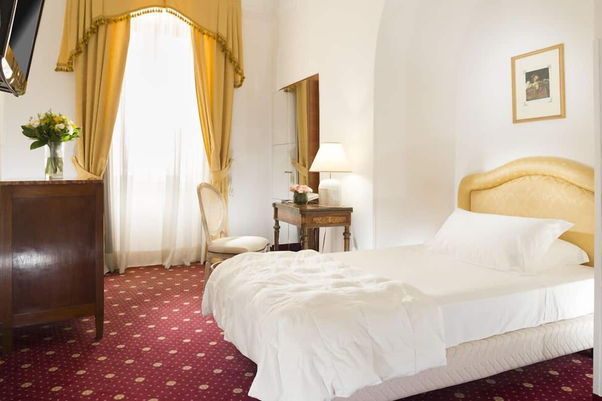 A hotel room with a bed, a desk, a chair, a lamp, and a picture on the wall.