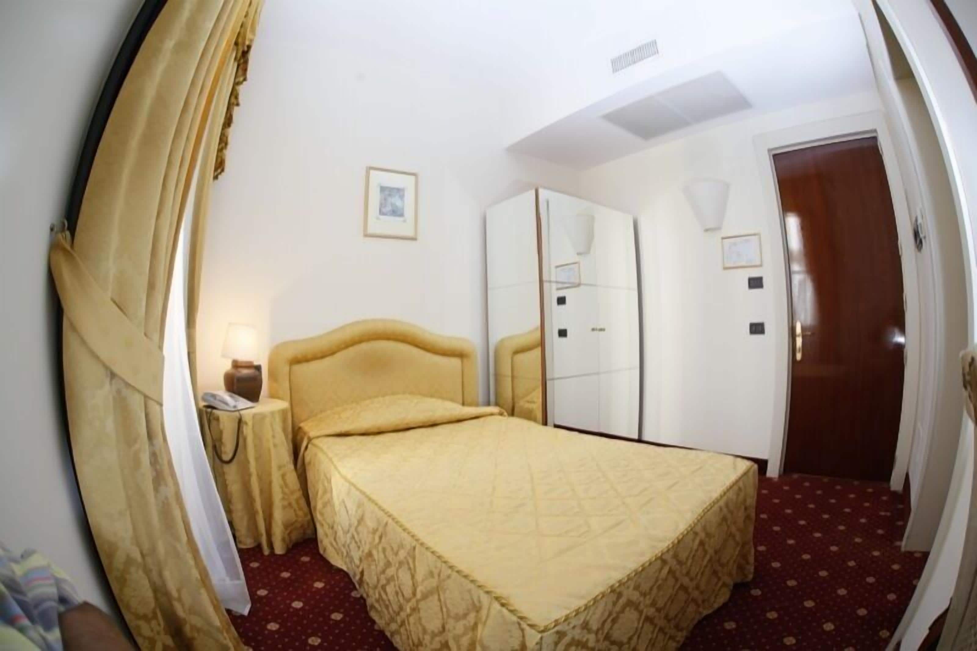 Una habitación de hotel con cama, mesita de noche, armario y puerta.