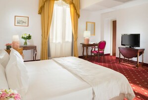 Una habitación de hotel con una cama grande, un escritorio con una silla, un televisor y una ventana con cortinas.