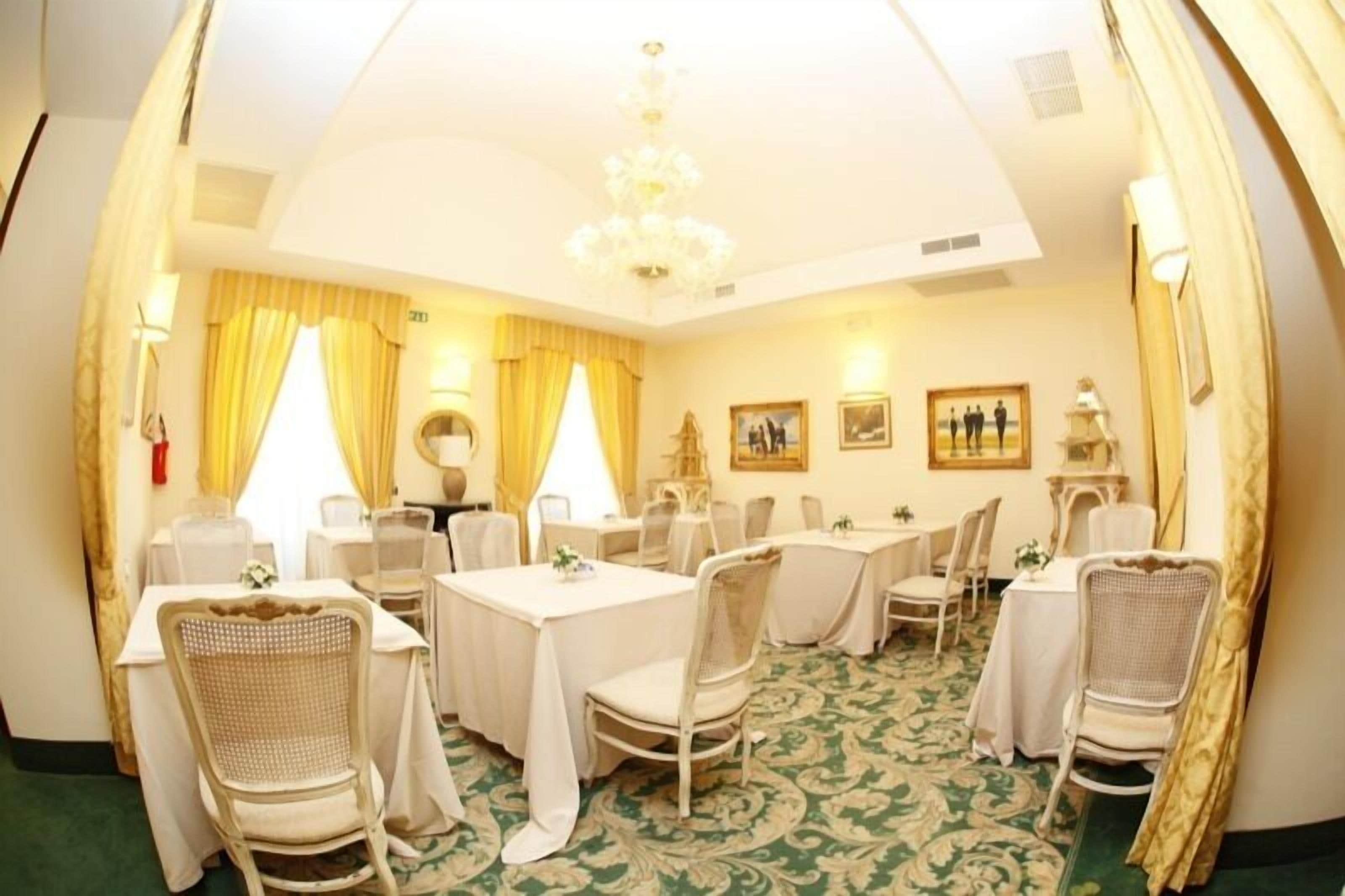 A hotel dining room with tables set for service, chandeliers, and framed artwork on the walls.