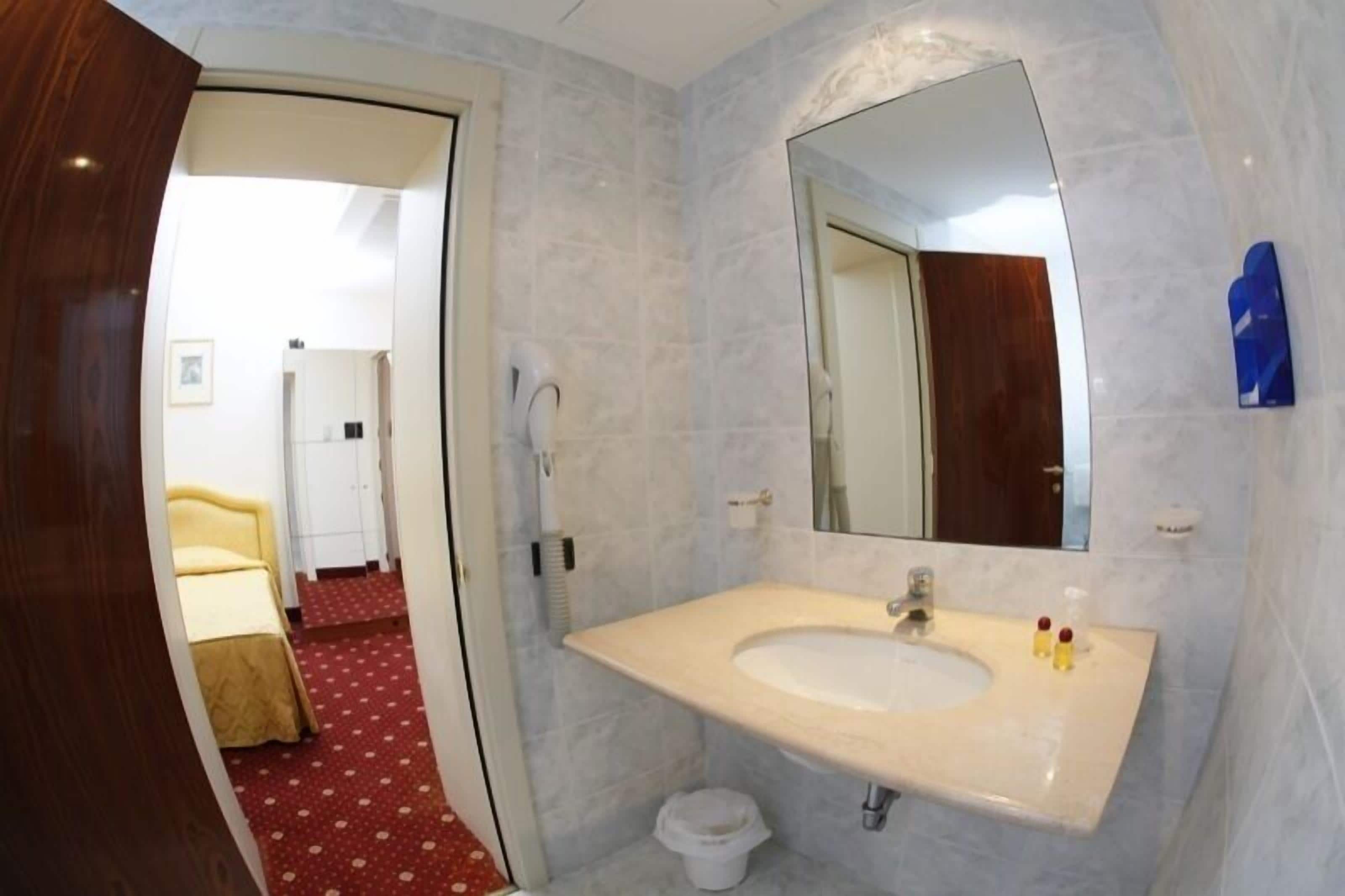 A hotel bathroom with a marble sink, a large mirror, and a red carpeted floor.
