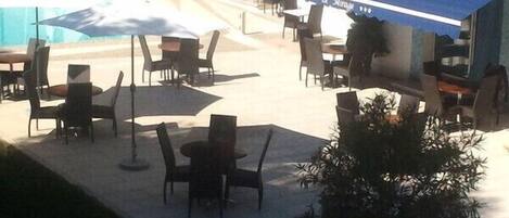 An outdoor seating area with tables and chairs, umbrellas, and a building with signage.