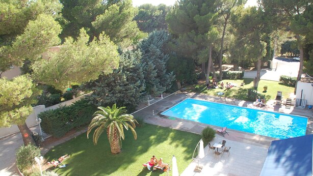 A swimming pool surrounded by lush greenery, with a patio area and lounge chairs. - Citotel Le Mirage (Istres)