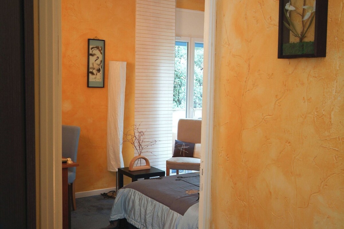 A bedroom with a bed, a chair, a nightstand, a window with blinds, and a door.