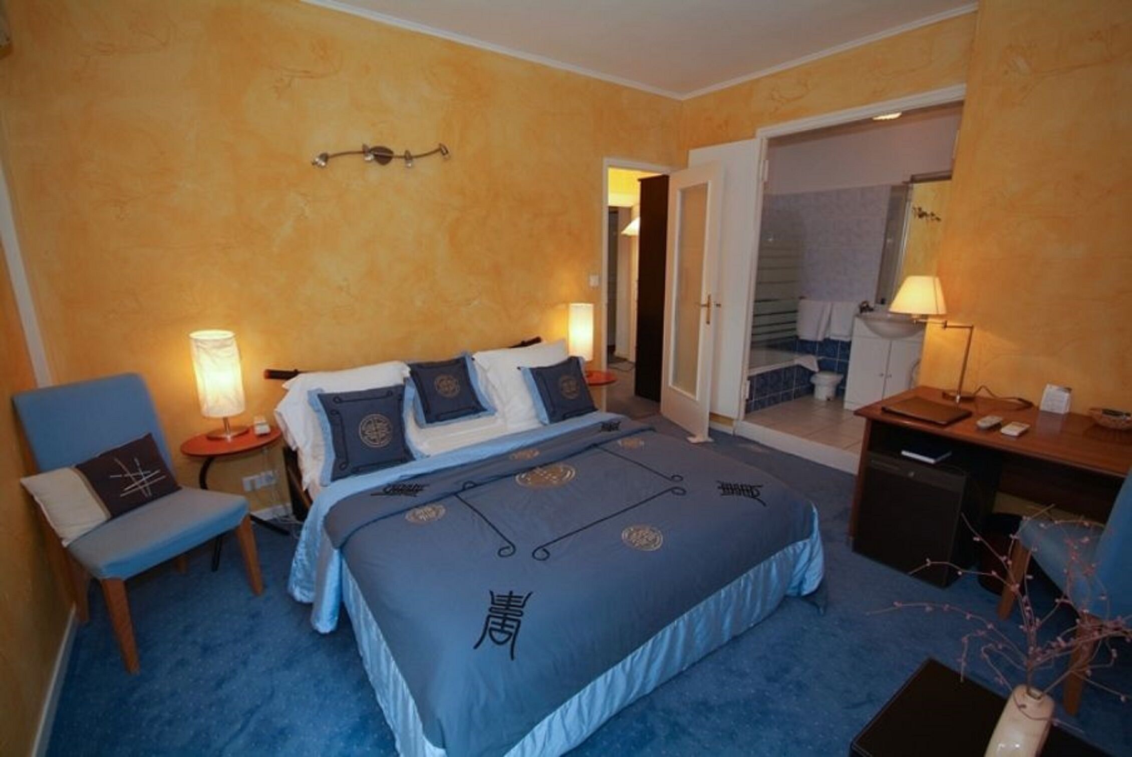 Habitación de hotel con cama, escritorio, silla y baño a la vista a través de una puerta abierta.