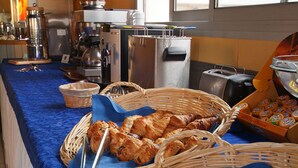 A buffet setup with various breads and pastries, a coffee machine, and a window with a view of trees. - Citotel Le Mirage (Istres)