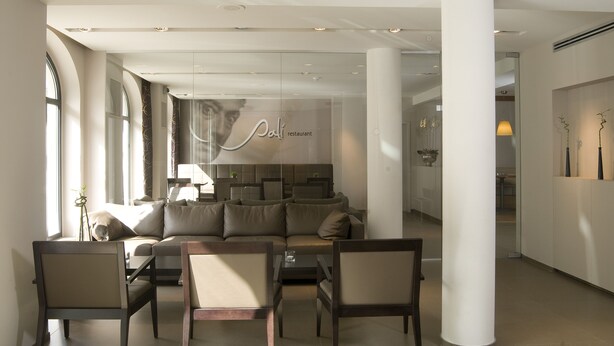 Una sala de estar moderna con un sofá, sillas y un muro de cristal que muestra el letrero de un restaurante.